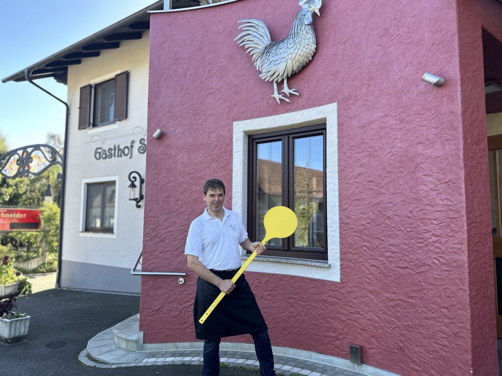 Hans-Peter mit einem großen Kochlöffel vor der Backhendlstation